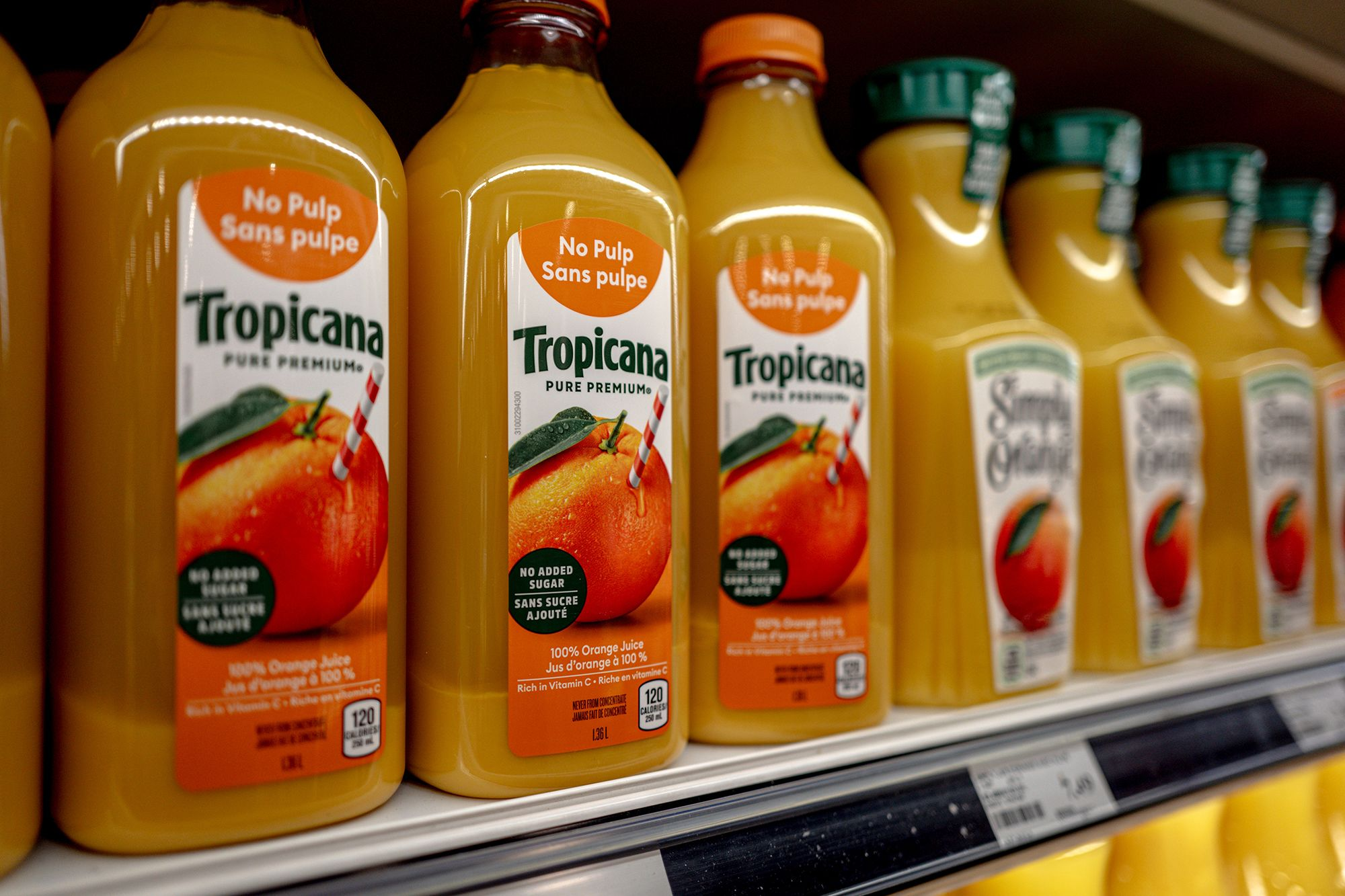 Garrafas de suco de laranja Tropicana na prateleira de supermercado, destaque para o rótulo que informa 'No Pulp'. Produto 100% natural, sem adição de açúcar, embalagem de 120ml, ideal para consumo saudável.